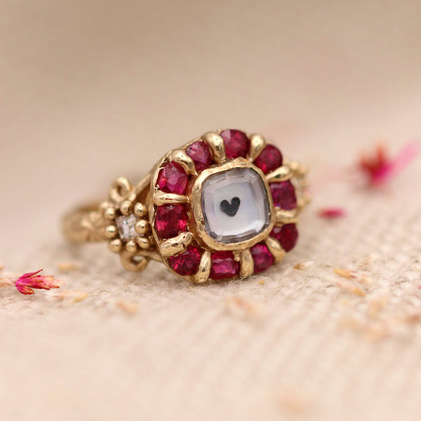 red ruby ring with a heart in the center, sitting on white fabric
