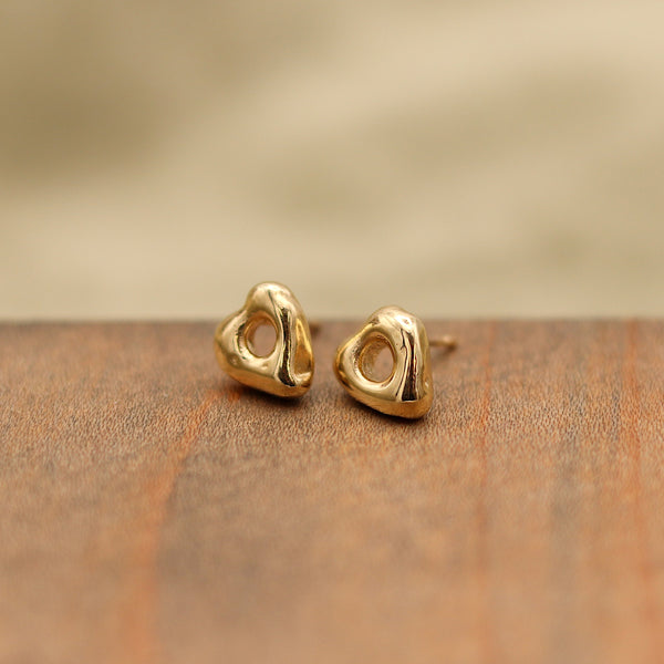 Gold heart-shaped earrings on a wooden surface with a beige background