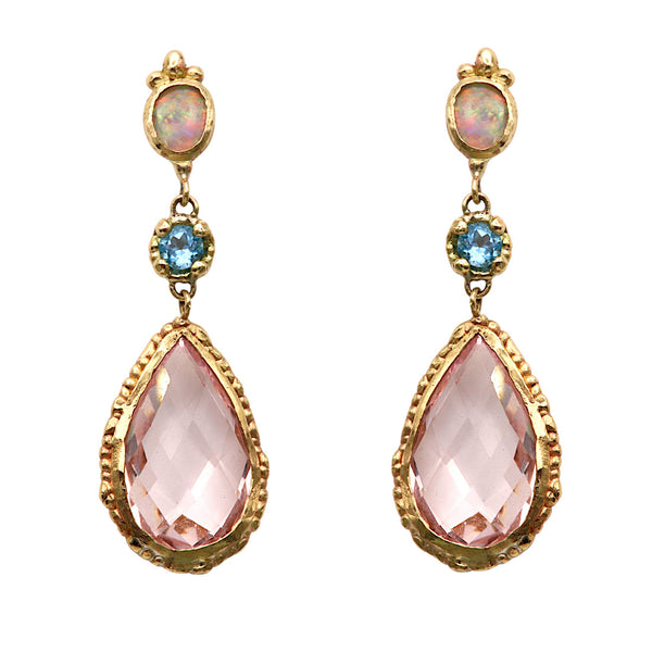 A pair of gold drop earrings featuring a large faceted pink teardrop gemstone, a smaller round blue gemstone, and an oval iridescent opal-like stone in an ornate gold setting, shown against a plain white background.