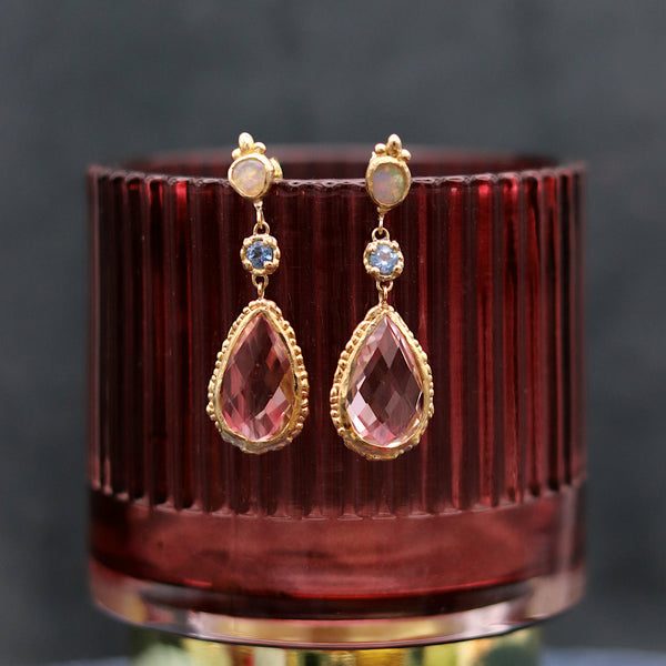 Pink and blue drop earrings displayed on a red glass cup against a blue backdrop
