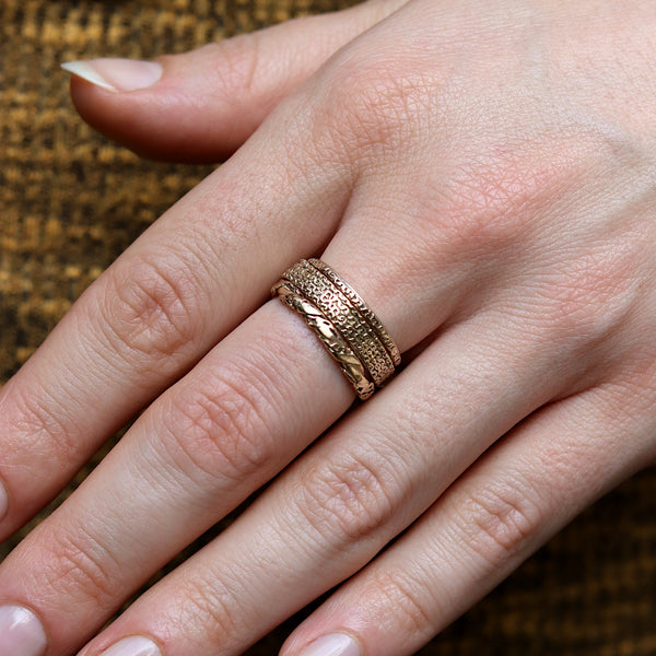 A close-up of a hand wearing three textured and twisted gold rings.