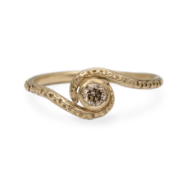 A gold ring with a textured, swirling band and a small round brown gemstone in the center, set against a plain white background.