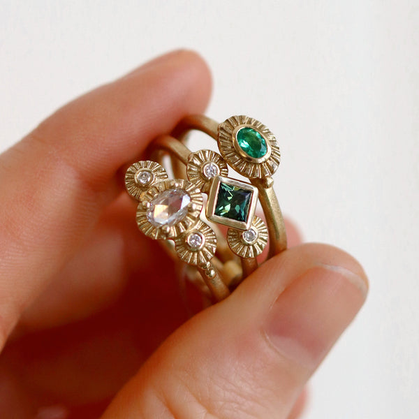 Gold rings with green and white 
gemstones held in a hand against a white background