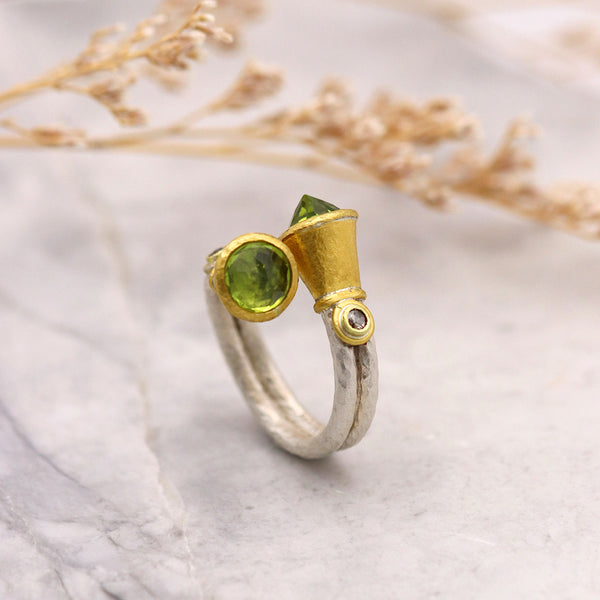 a crossover ring with green gemstones and gold accents on a marble surface with dried plants.